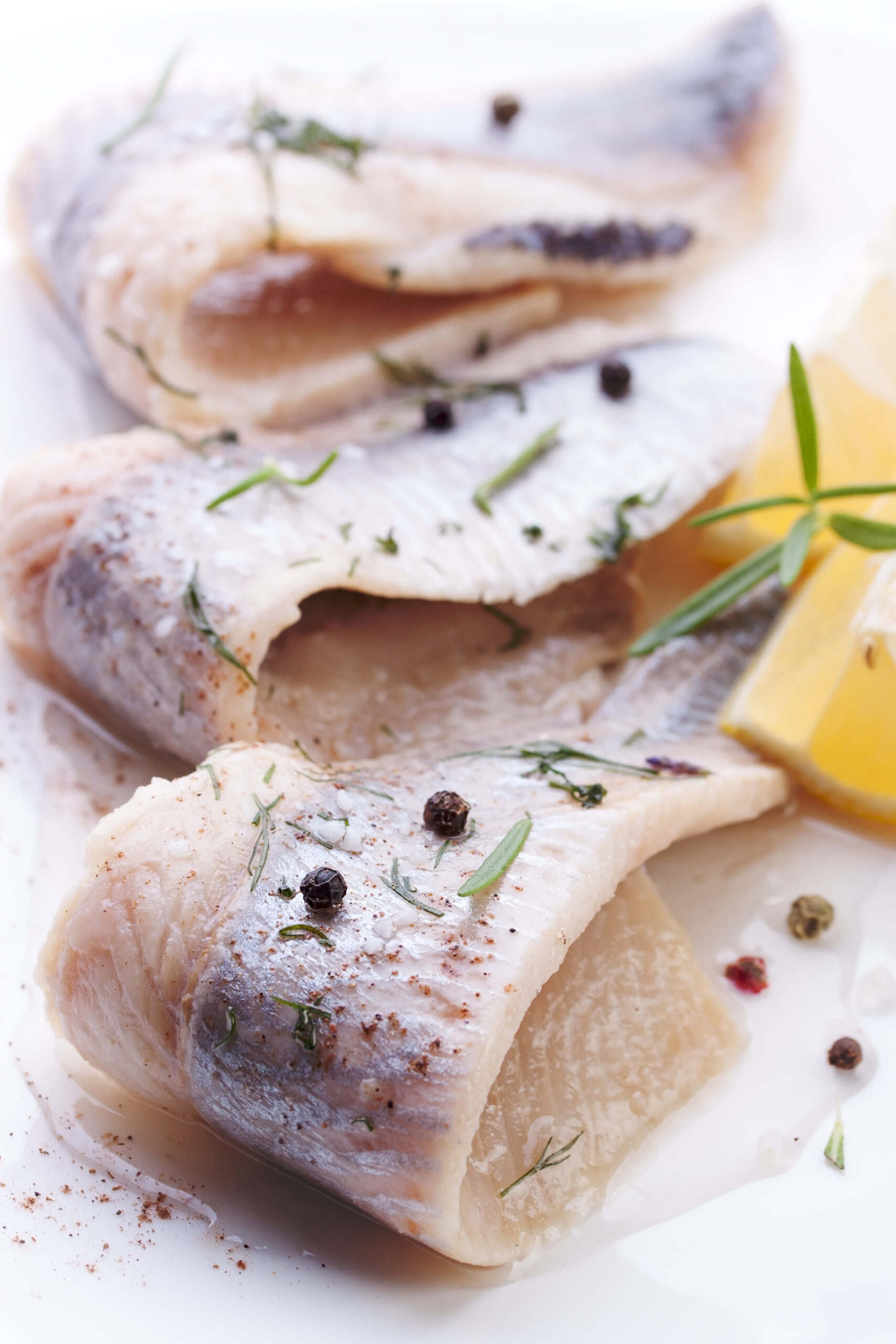Herring with salt, pepper, herbs and lemon on white ceramic plate on white background