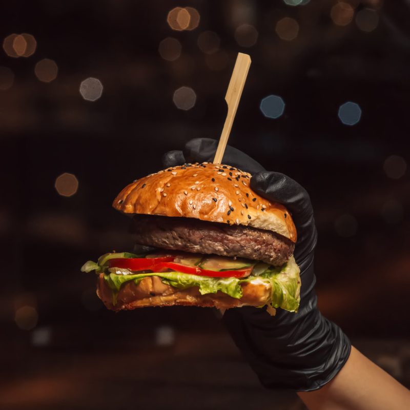 hand in burger gloves holding beef burger in black background