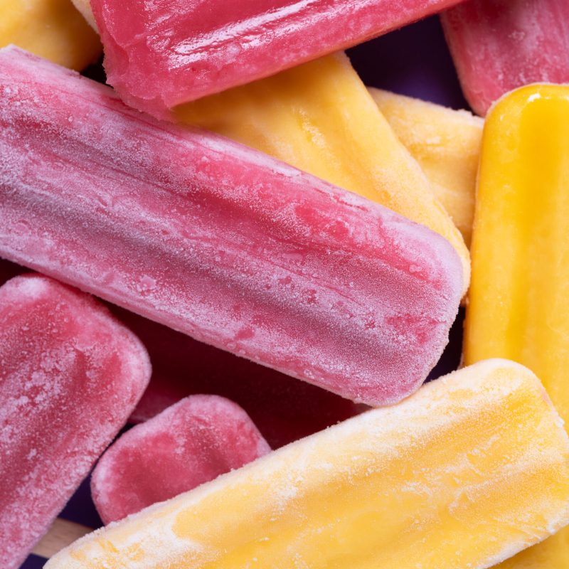 Red strawberry popsicles and yellow popsicles on purple background