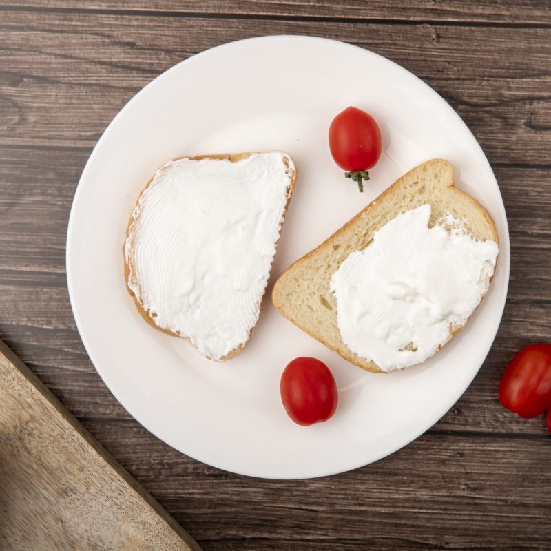 top view of plate with bread slices smeared with cottage cheese and tomatoes on wooden background
